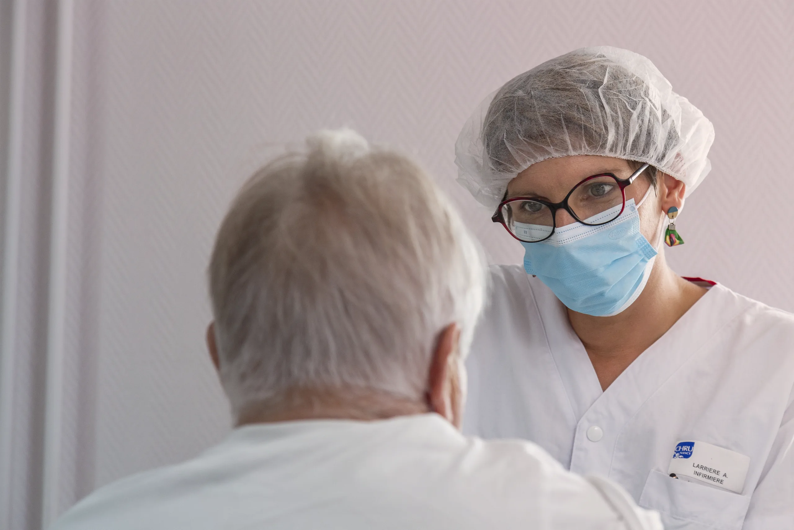 Infirmière en tenue de bloc, charlotte et masque, échangeant avec un patient âgé dans un service hospitalier